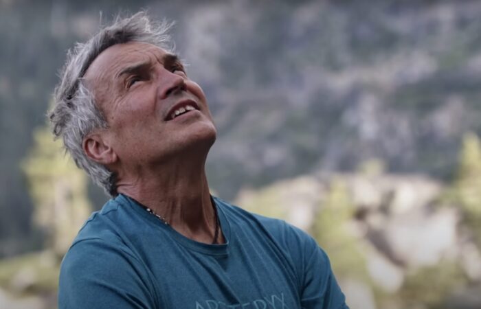 gray-haired man looking up at a mountain face